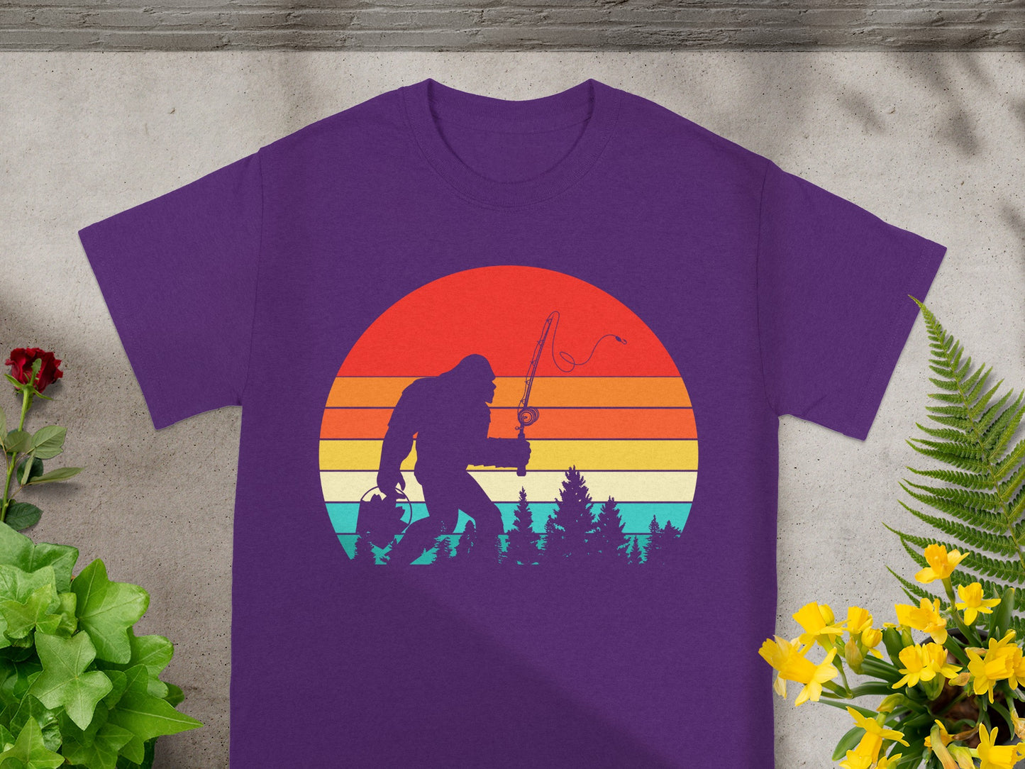 Bigfoot silhouette fishing against a retro striped sunset on a purple t-shirt.