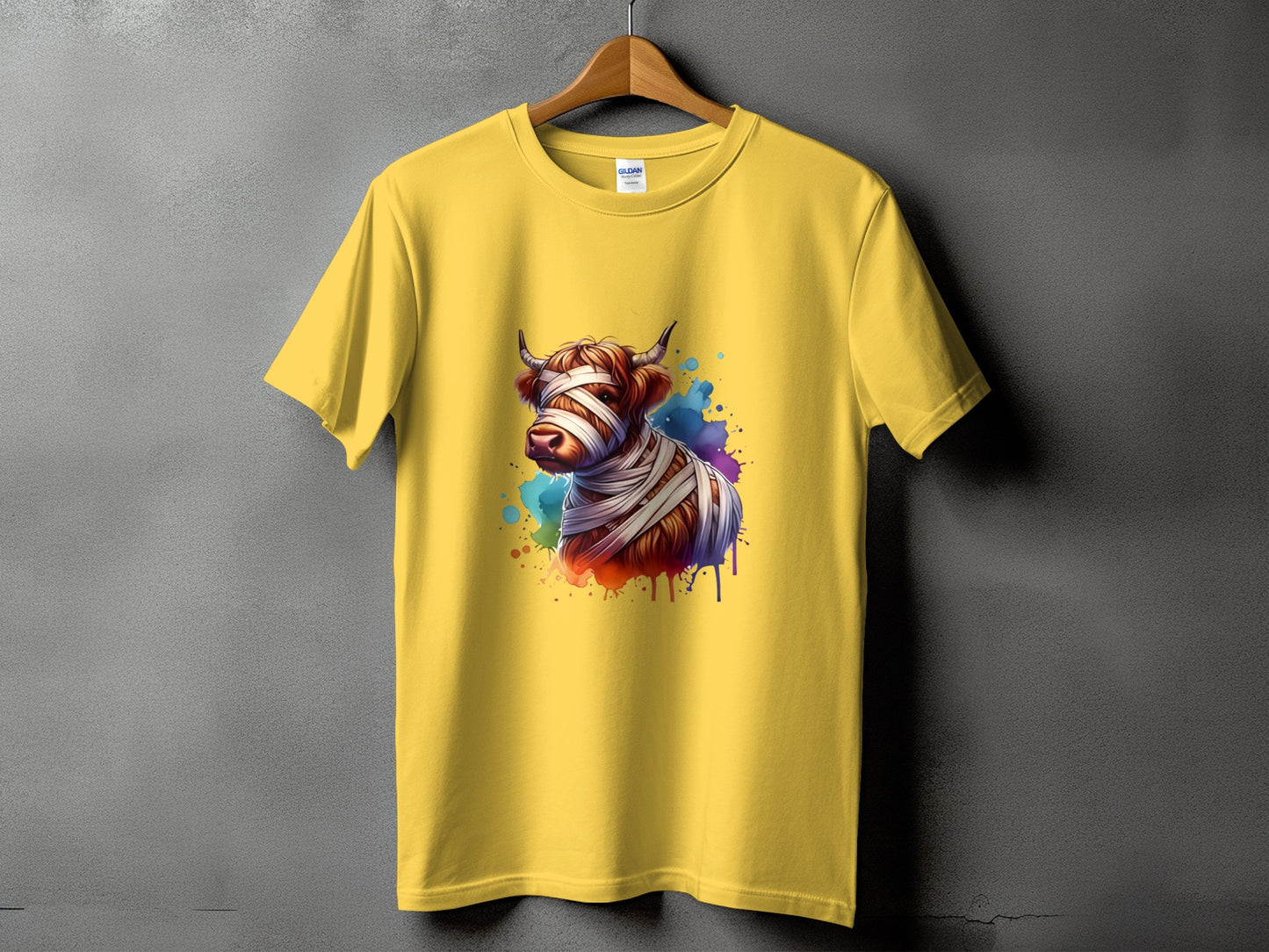 Yellow t-shirt with a graphic of a Highland cow wrapped in bandages with watercolor splatters.