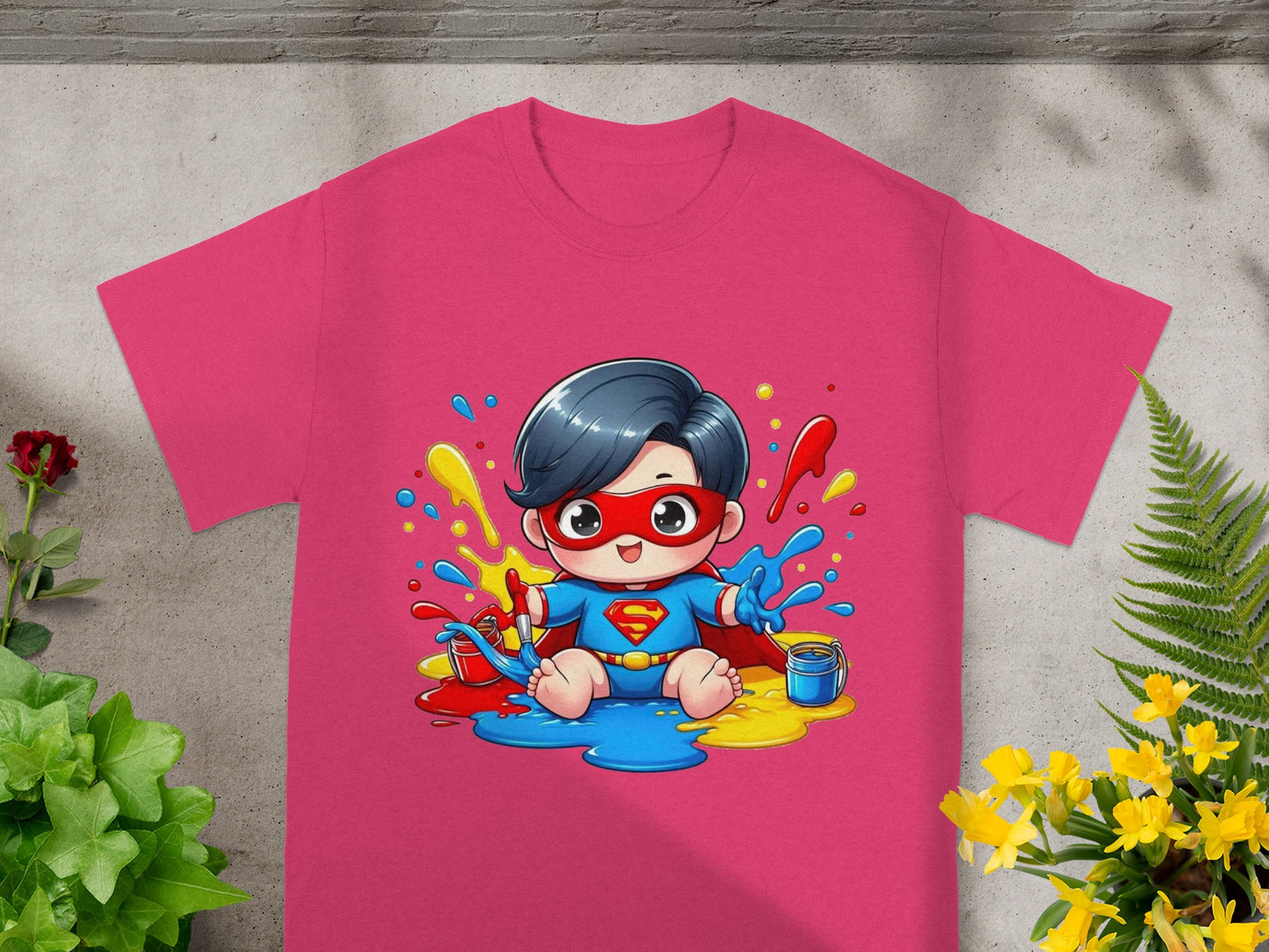 Pink t-shirt with cartoon superhero child sitting in colorful paint splatters.