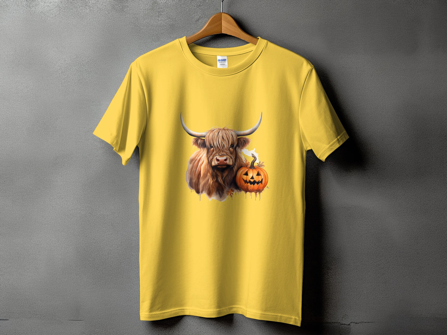 Yellow t-shirt featuring a Highland cow and jack-o'-lantern graphic with leaves.