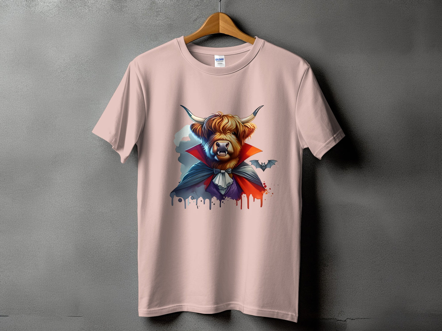 Highland cow wearing a vampire cape and bat illustration on a pink t-shirt.