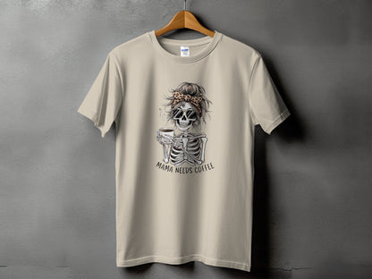 Skeleton graphic with "Mama Needs Coffee" text on a light tan t-shirt.