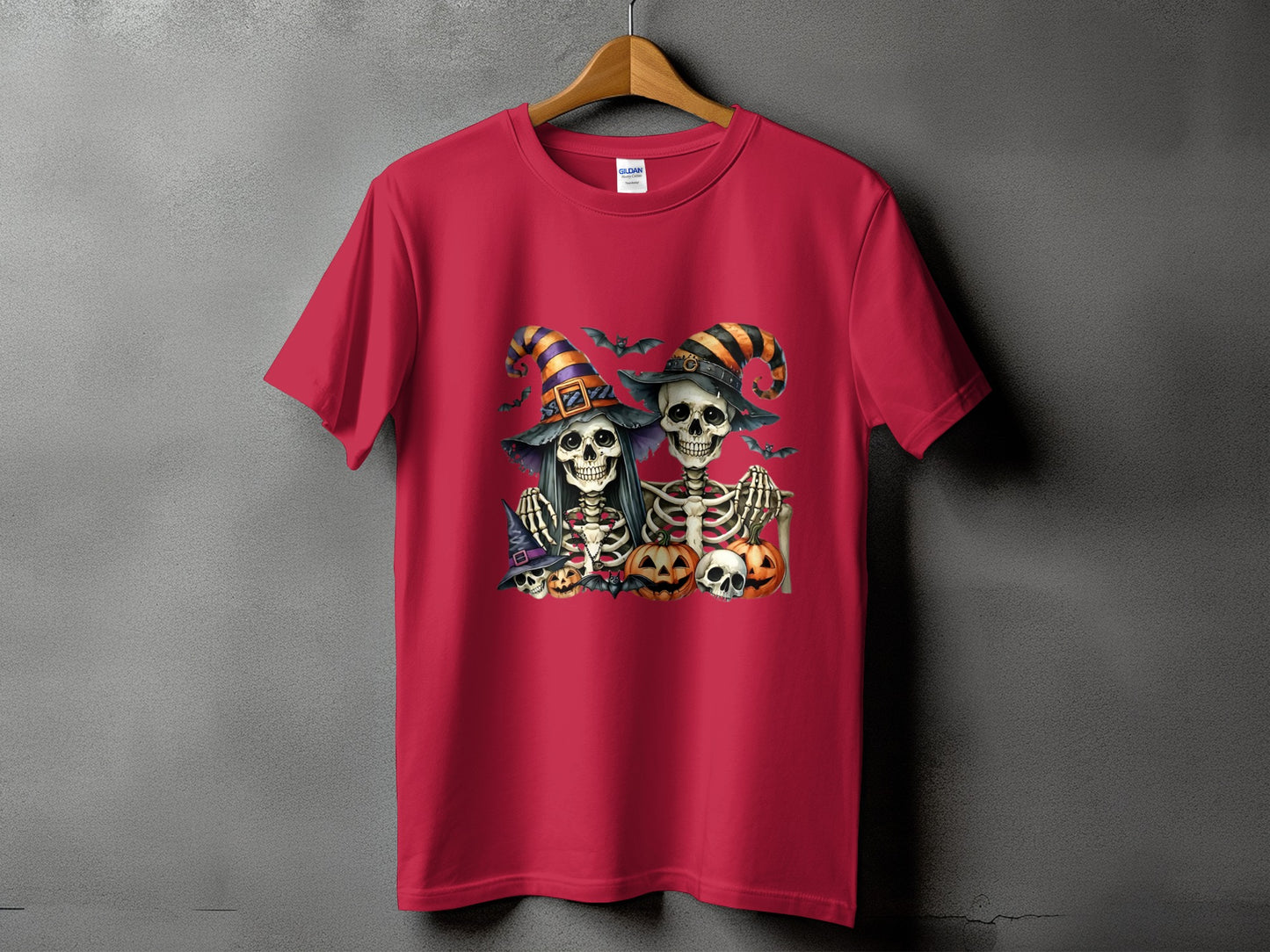 Two skeletons in witch hats with bats and pumpkins on a red t-shirt.