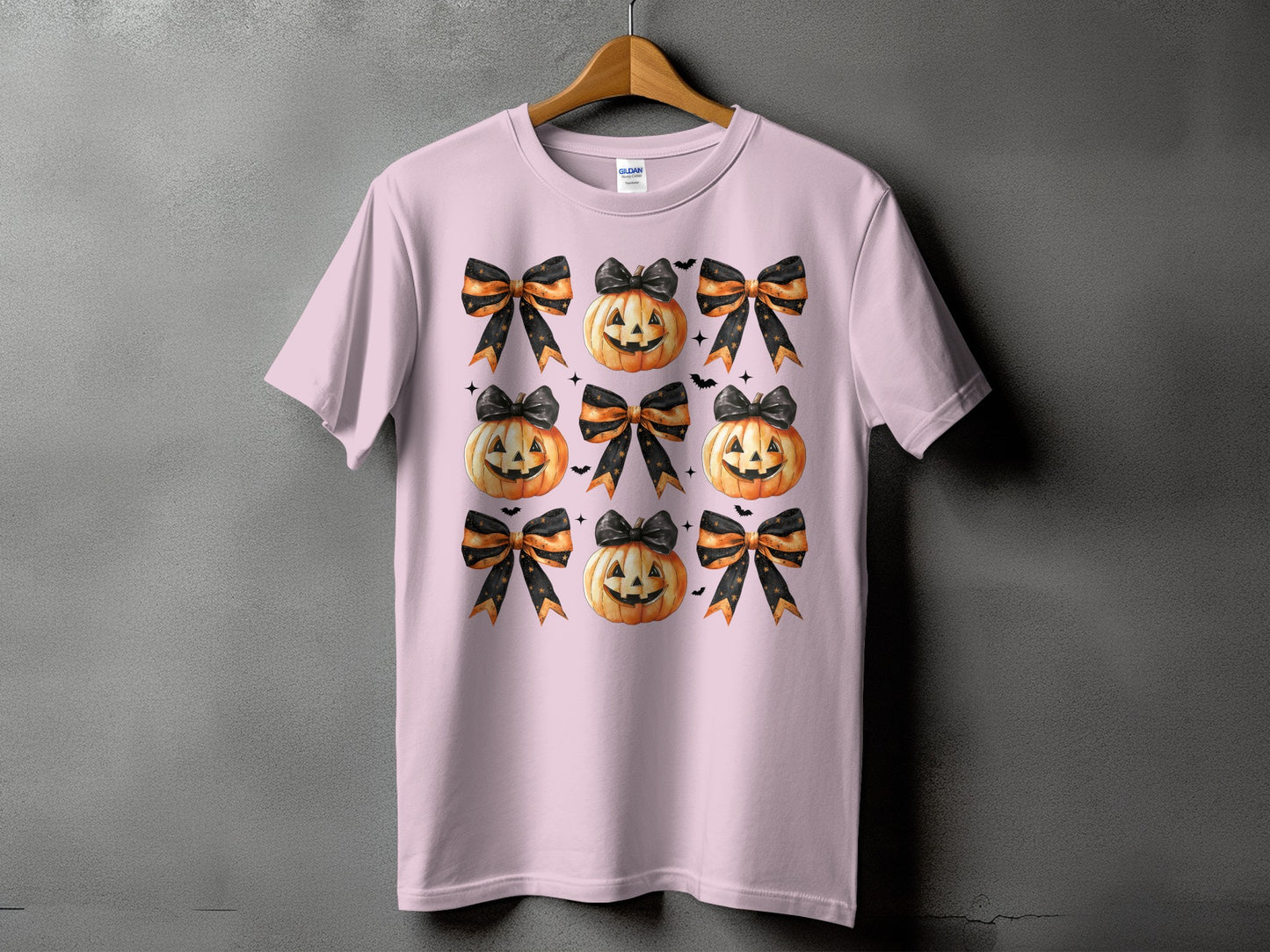Pink t-shirt with a repeated pattern of Halloween pumpkins and bows.