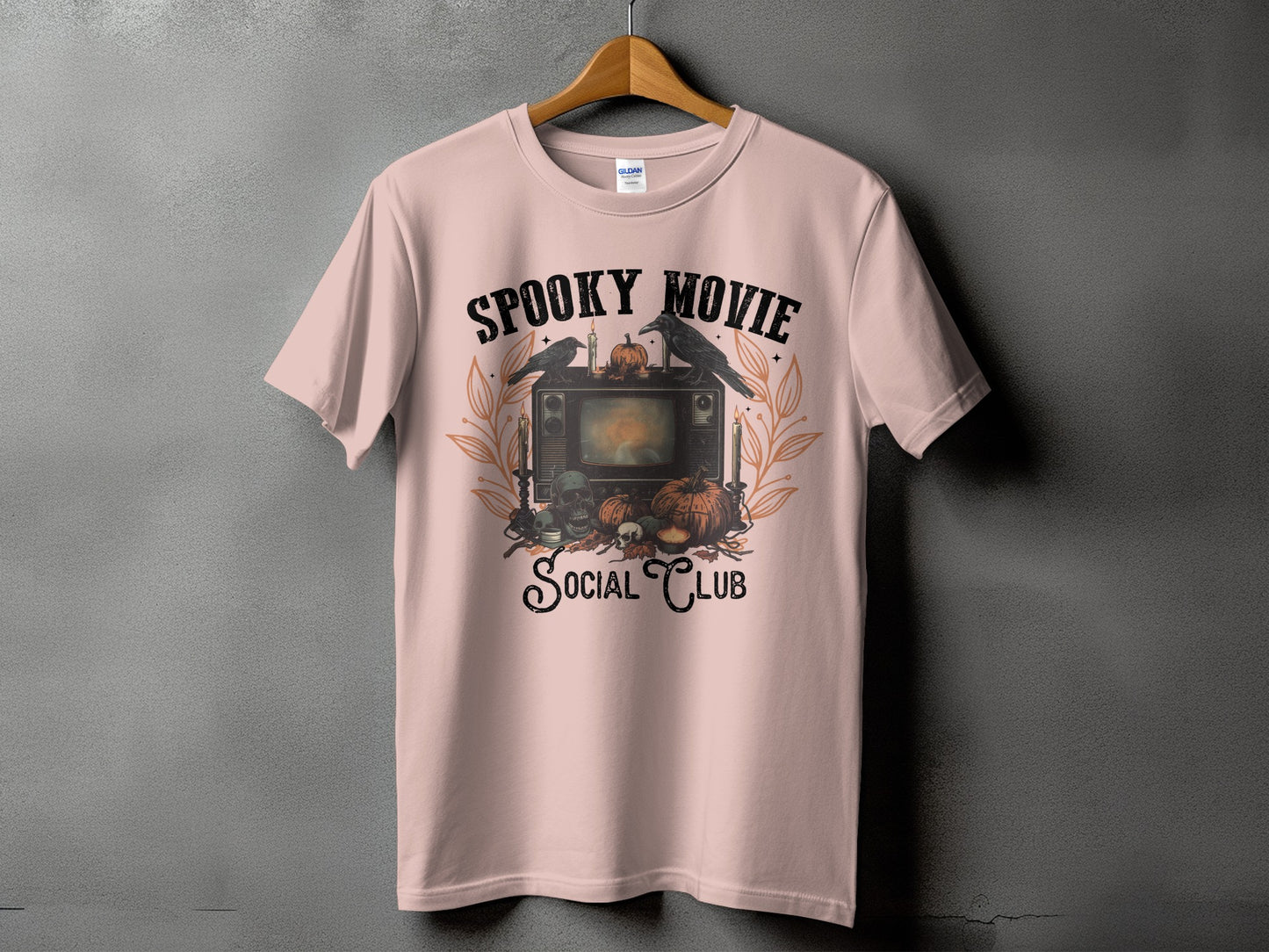 Pink t-shirt with "Spooky Movie Social Club" graphic featuring a vintage TV, crows, pumpkins, and skulls.