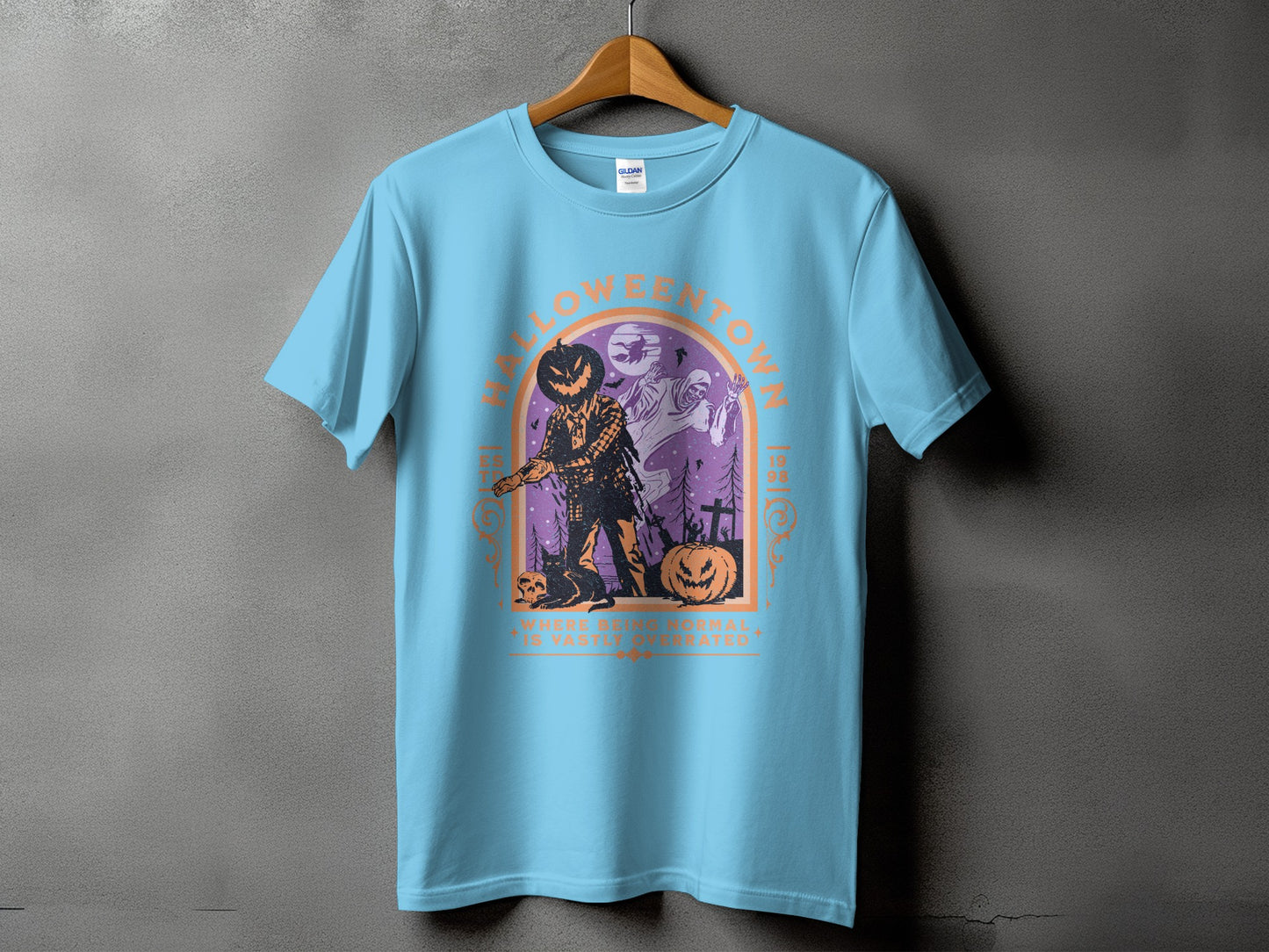 Light blue t-shirt with "HALLOWEENTOWN" and spooky graphics, text reads "WHERE BEING NORMAL IS VASTLY OVERRATED".