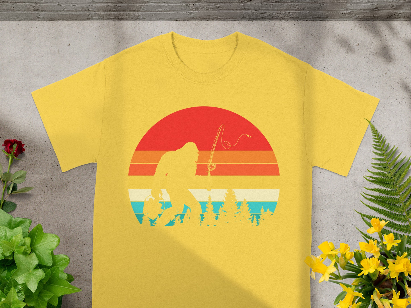 Yellow t-shirt with Bigfoot fishing silhouette against a retro sunset and trees.