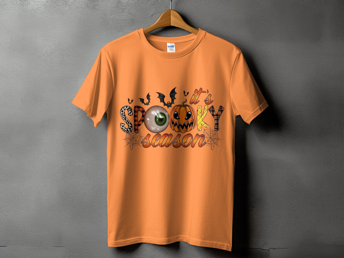 Orange t-shirt with "It's Spooky Season" Halloween graphic featuring bats, eye, and pumpkin.