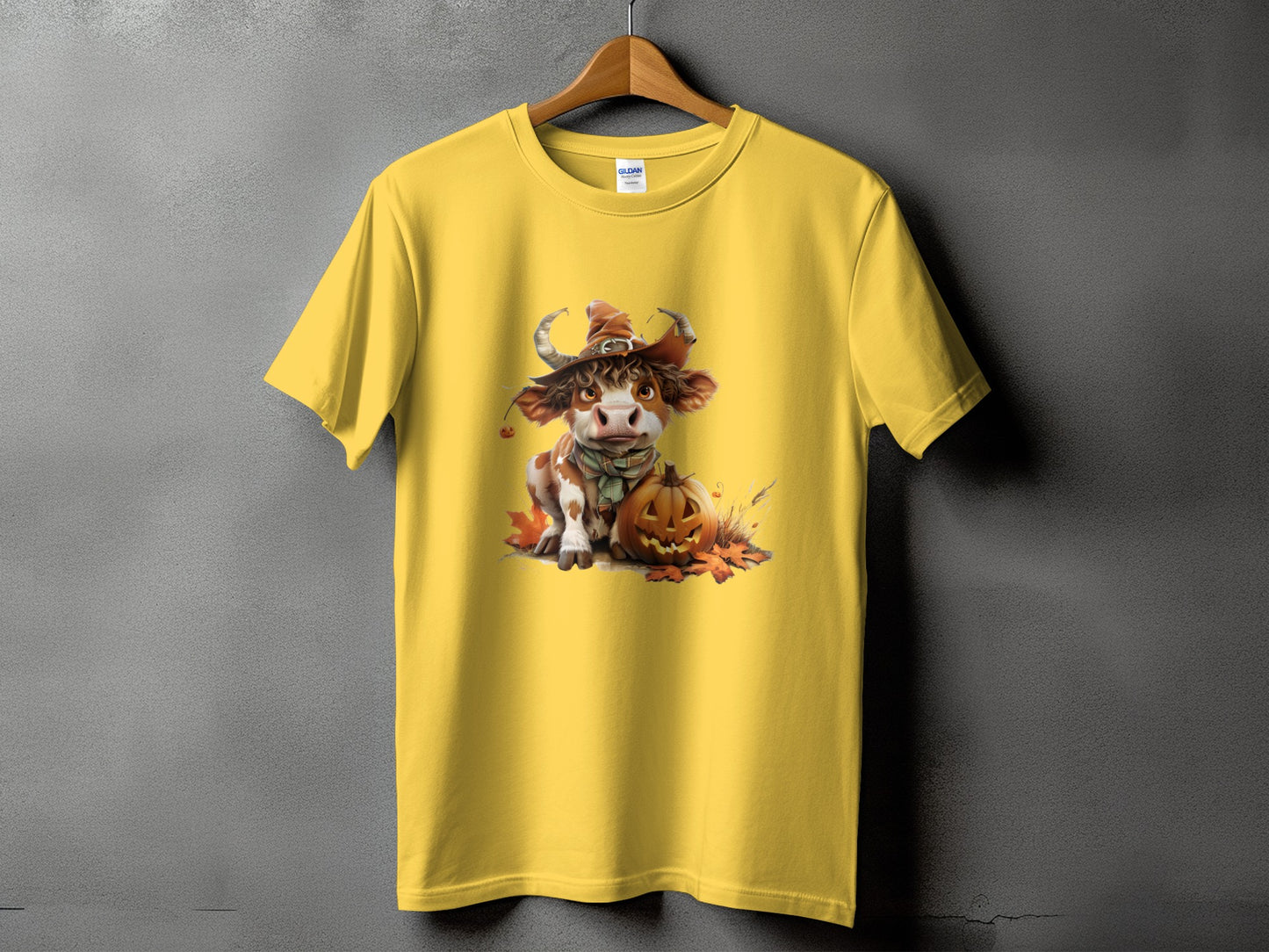 Yellow t-shirt with a cartoon cow wearing a witch hat and a pumpkin.