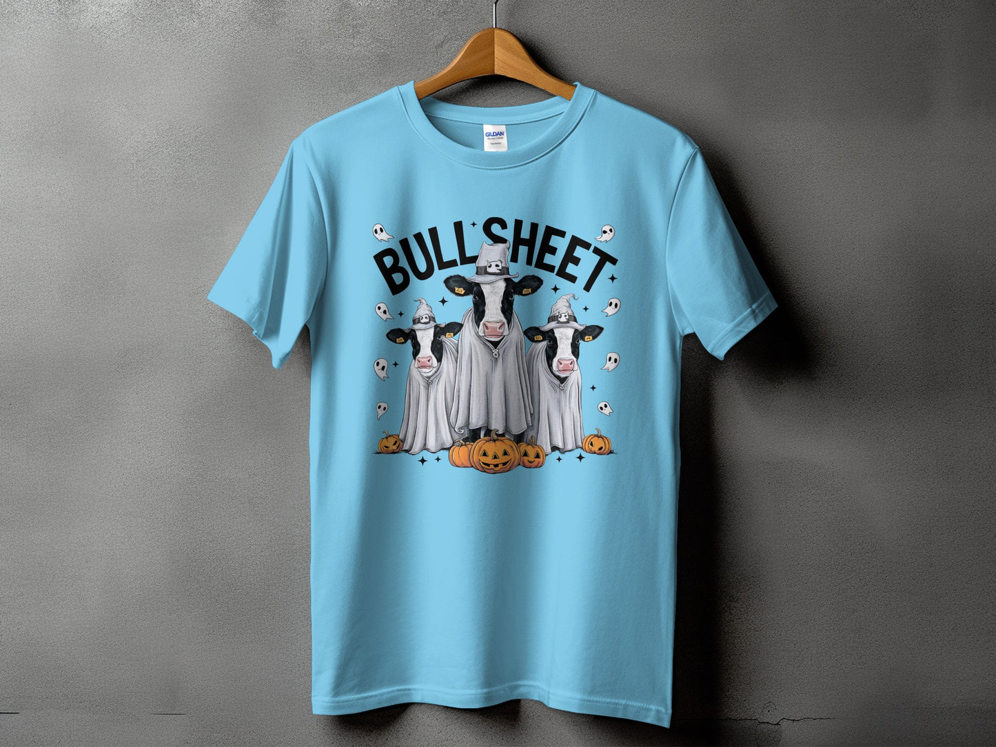 Light blue t-shirt with graphic of three cows in ghost costumes and pumpkins.