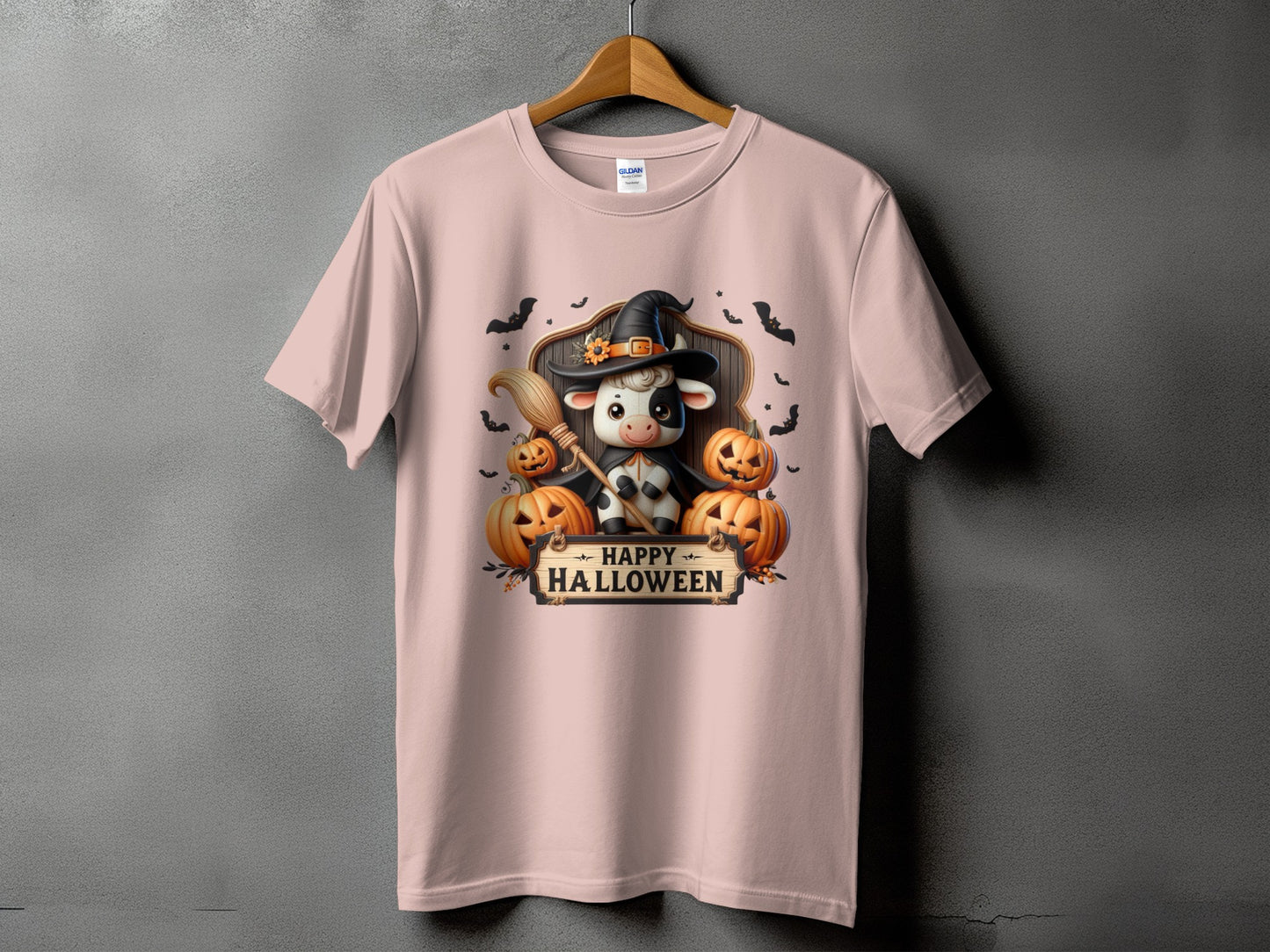 Pink t-shirt with a cow in a witch hat holding a broom, surrounded by pumpkins.
