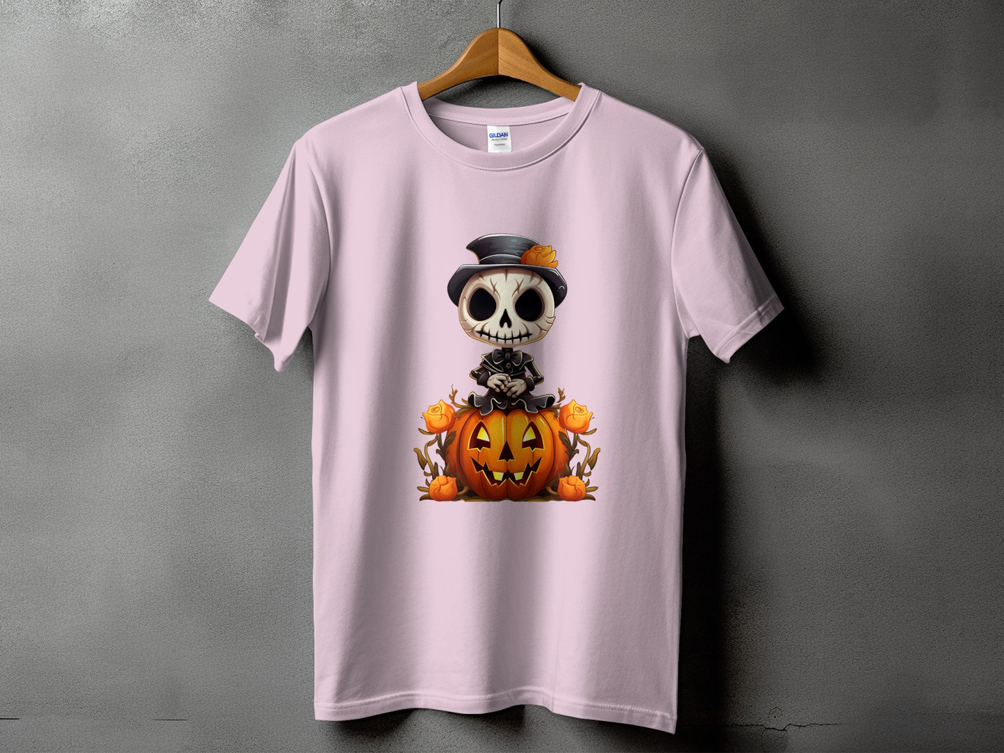 Light pink t-shirt with a skeleton wearing a hat sitting on a pumpkin.