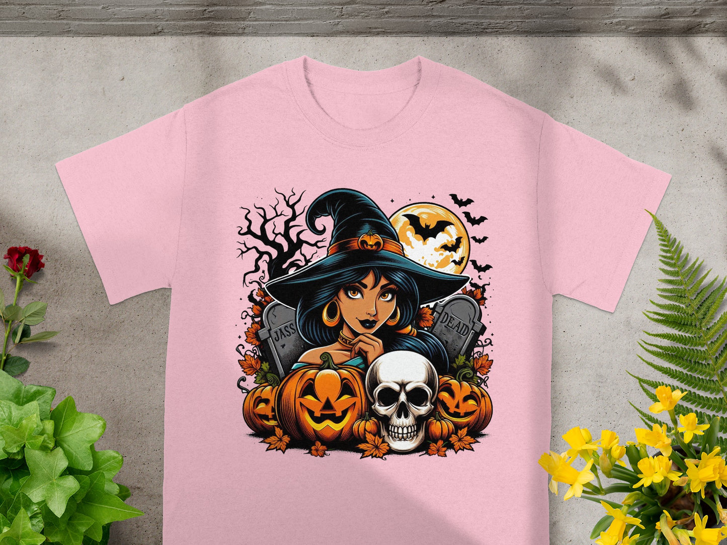 Halloween graphic on pink t-shirt with witch, pumpkins, skull, tombstones, and bats.