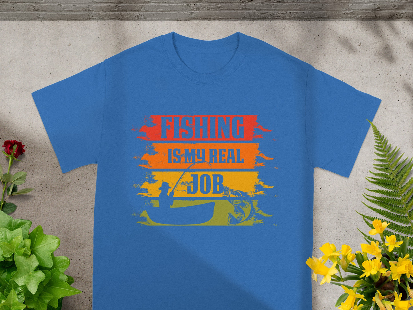 Blue t-shirt with "FISHING IS MY REAL JOB" text, silhouette of person fishing from boat, and fish.