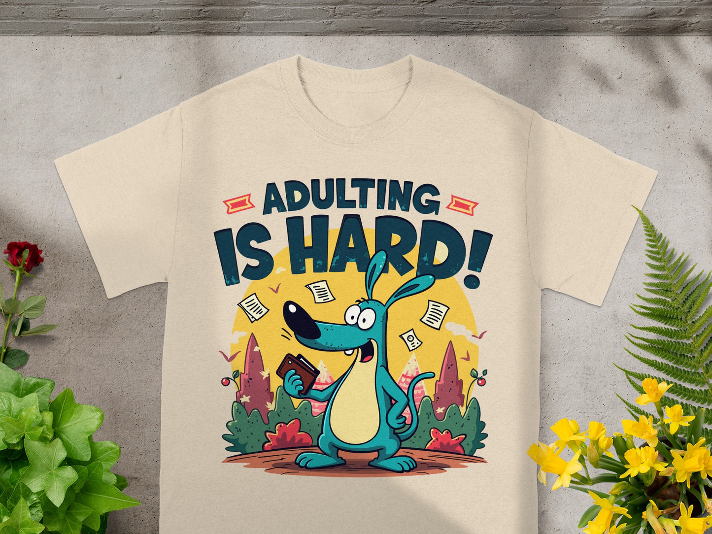 Blue cartoon dog on beige shirt with "ADULTING IS HARD!" text and falling papers.