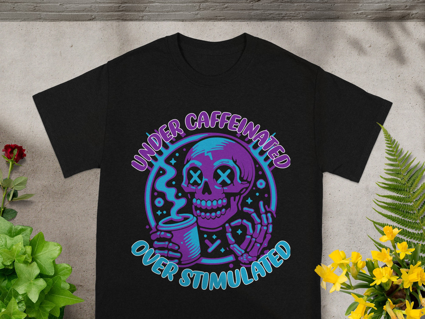 T-shirt with purple skeleton holding coffee, text "UNDER CAFFEINATED OVER STIMULATED".
