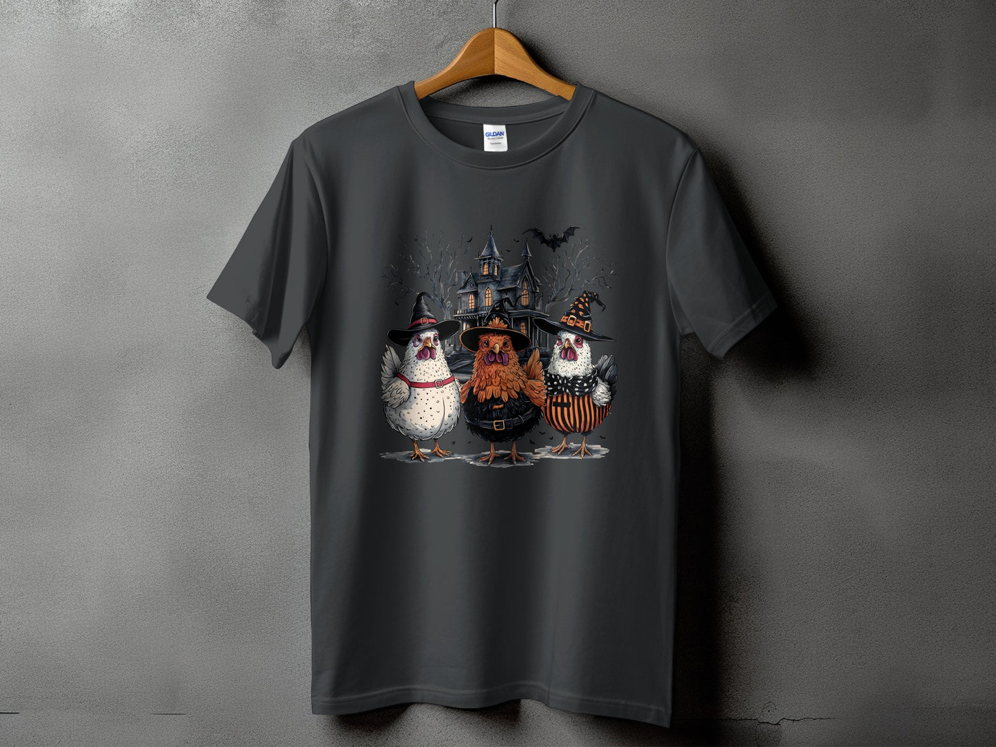 Three chickens in witch hats stand before a haunted house on a t-shirt.