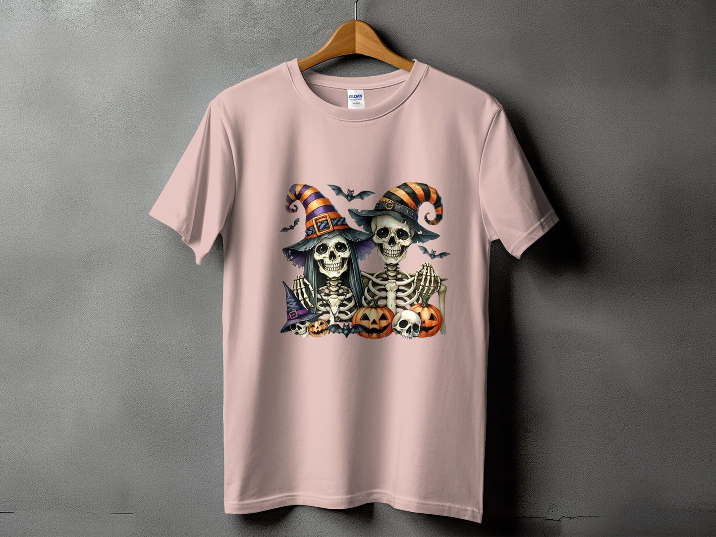 Two skeletons in witch hats with pumpkins and bats on a pink t-shirt.