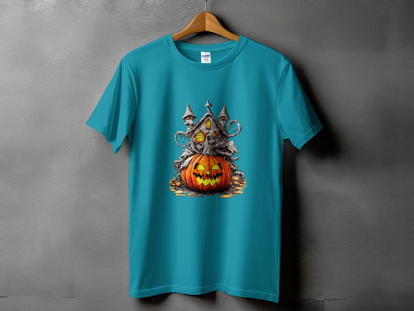 Teal t-shirt with a Halloween graphic of a haunted house on a jack-o'-lantern.