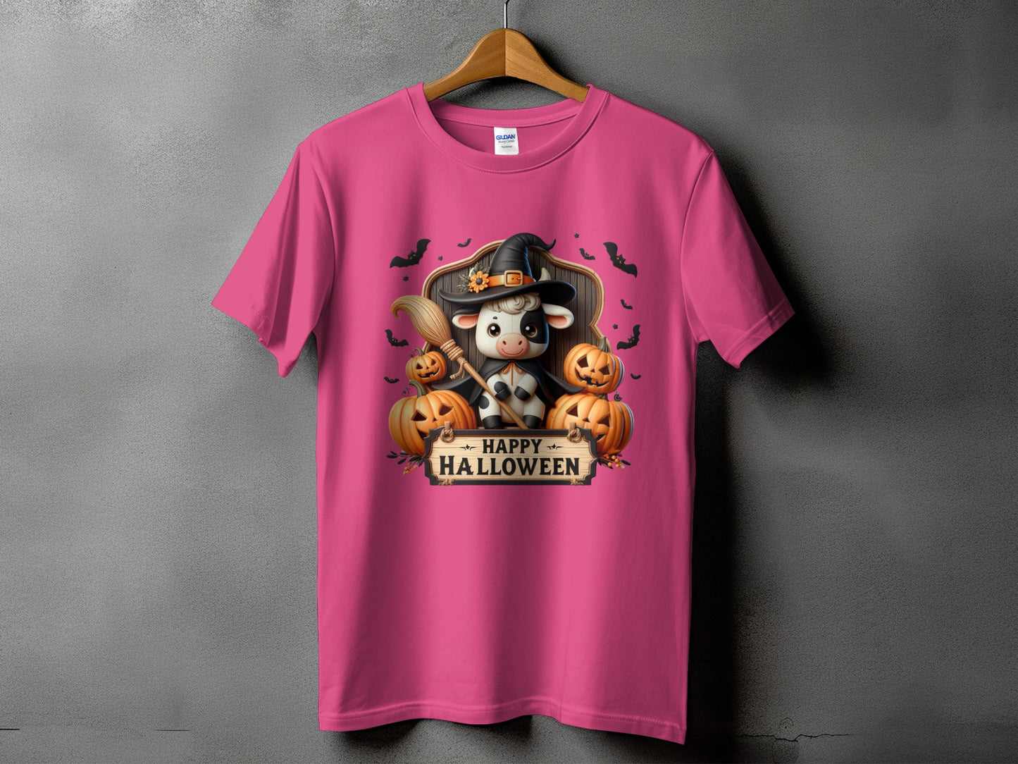 Pink t-shirt with a Halloween graphic of a cow wearing a witch hat, broom, and pumpkins.
