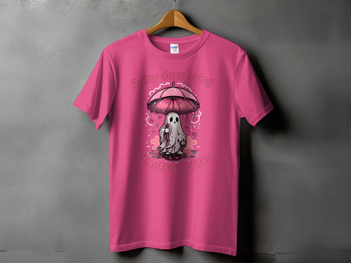 Pink t-shirt with a ghost holding an umbrella, text reads "Rainy days bring peaceful vibes".
