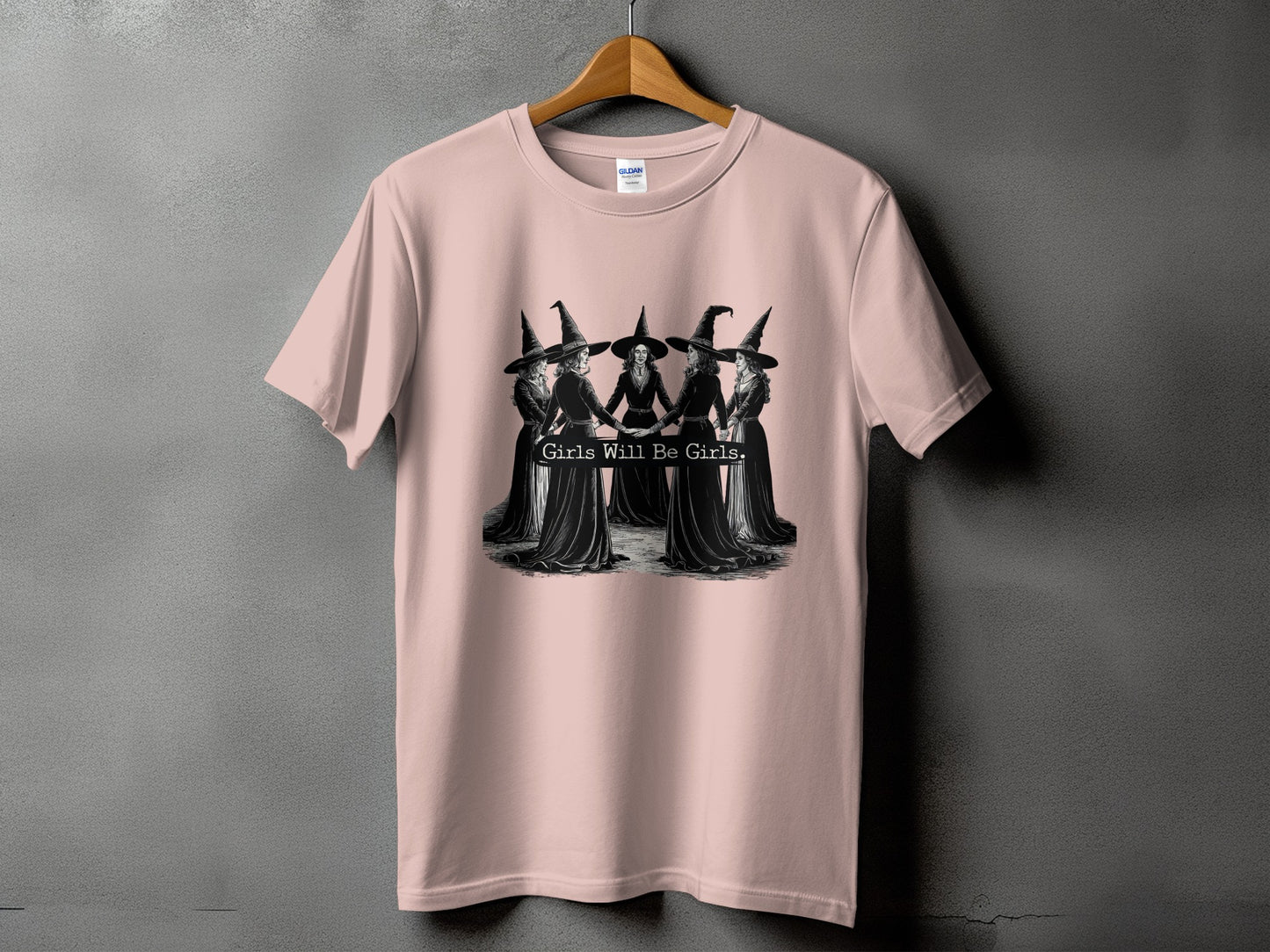 Pink t-shirt with a graphic of five witches holding hands and the text "Girls Will Be Girls."