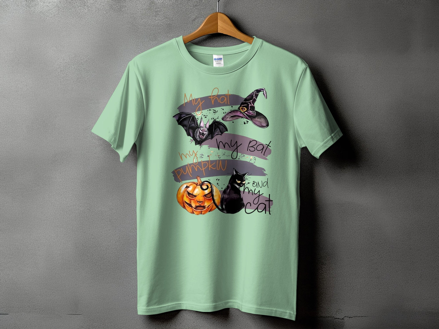 Light green t-shirt with Halloween graphics: hat, bat, pumpkin, black cat, and text.