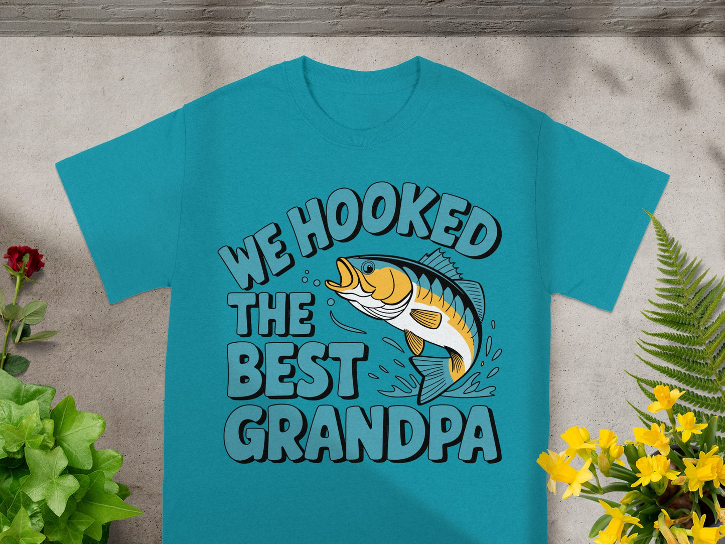 Teal t-shirt with text "We Hooked The Best Grandpa" and a leaping fish graphic.
