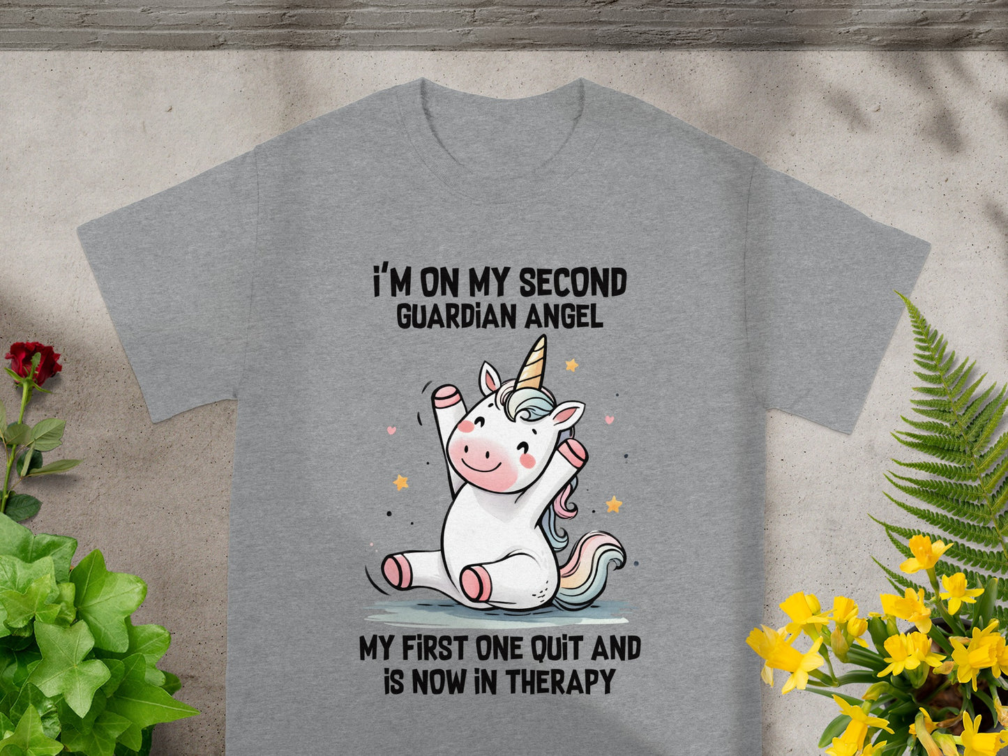 Gray t-shirt with illustration of unicorn and text: "I'M ON MY SECOND GUARDIAN ANGEL MY FIRST ONE QUIT AND IS NOW IN THERAPY."