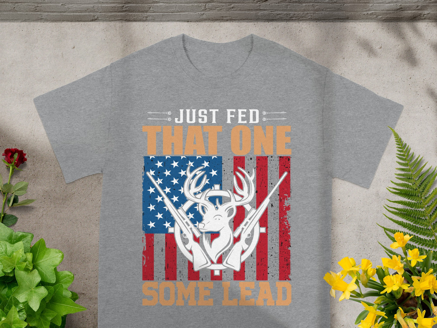 Grey t-shirt with deer, guns, and American flag graphic text "JUST FED THAT ONE SOME LEAD".