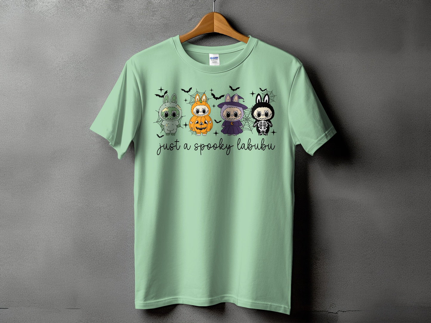 Light green t-shirt with four Halloween-themed cartoon characters and "just a spooky labubu" text.