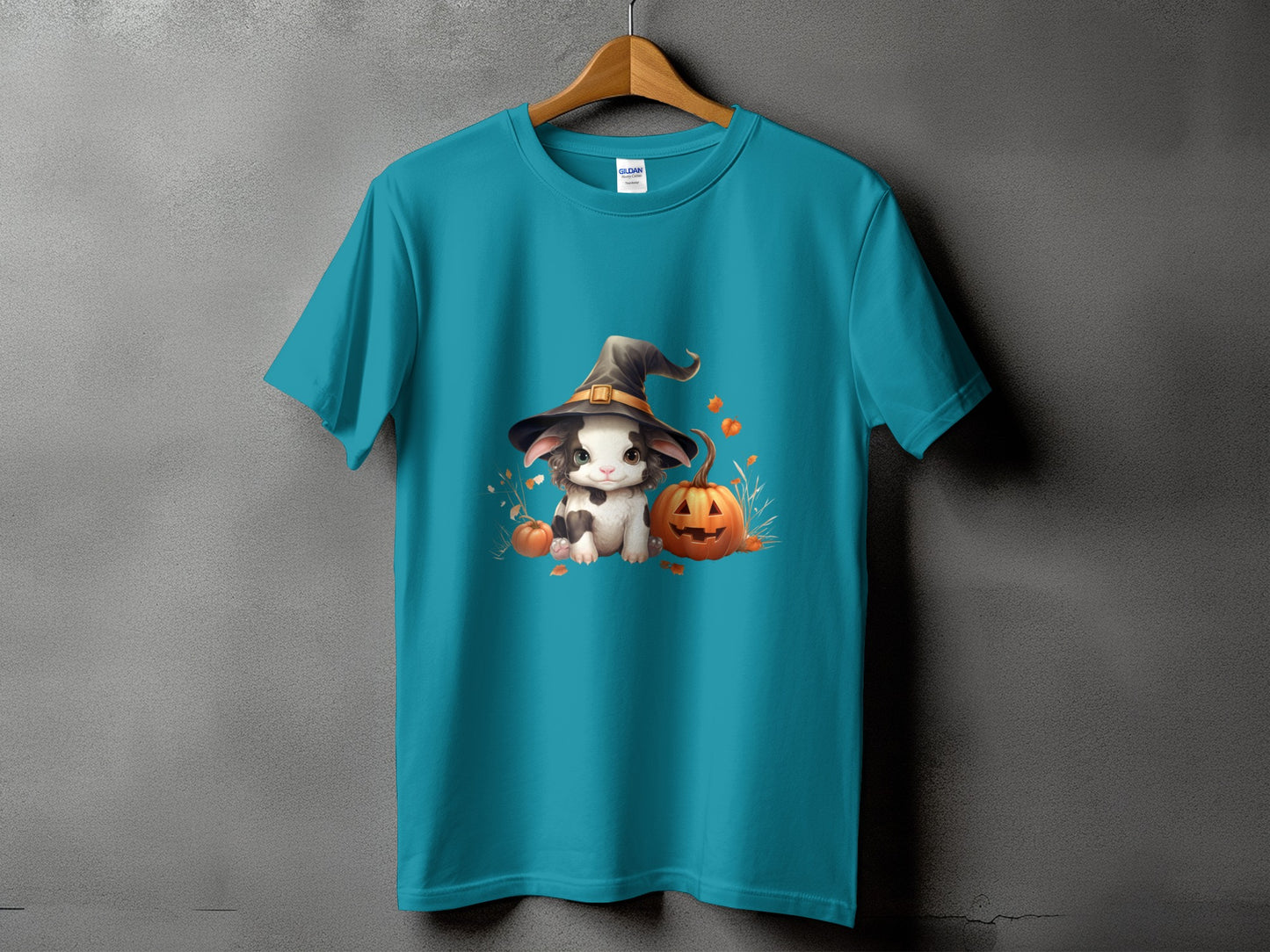 Teal t-shirt with a white kitten wearing a witch hat and surrounded by pumpkins.