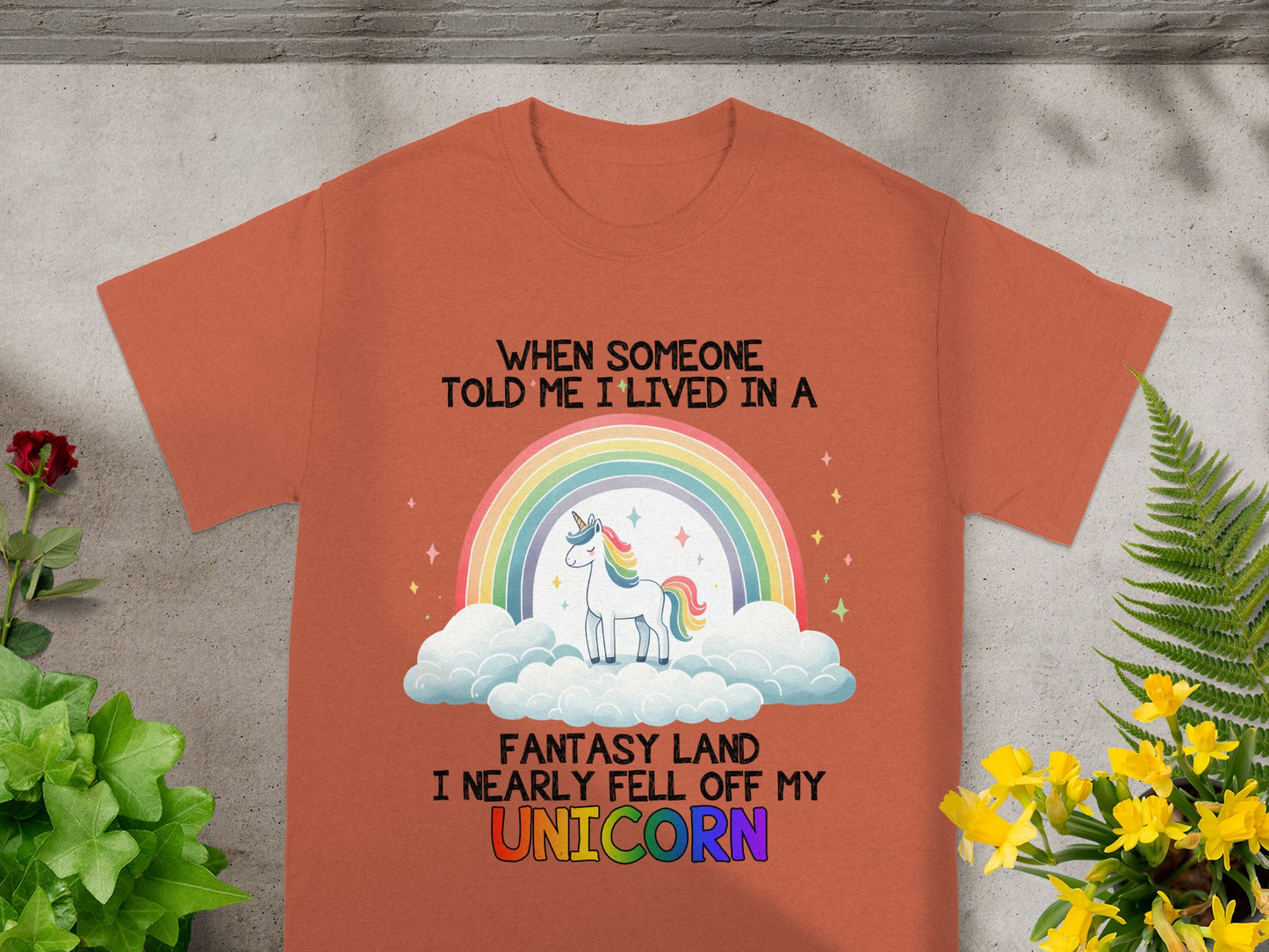 Orange t-shirt with a unicorn, rainbow, and the text "When someone told me I lived in a fantasy land I nearly fell off my unicorn."