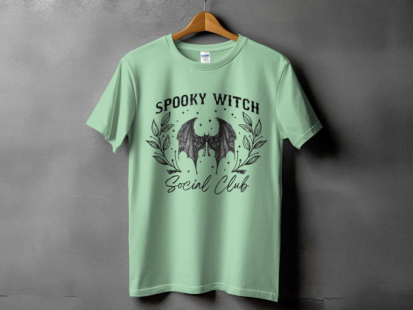 Green t-shirt with "Spooky Witch Social Club" text and bat wings graphic.