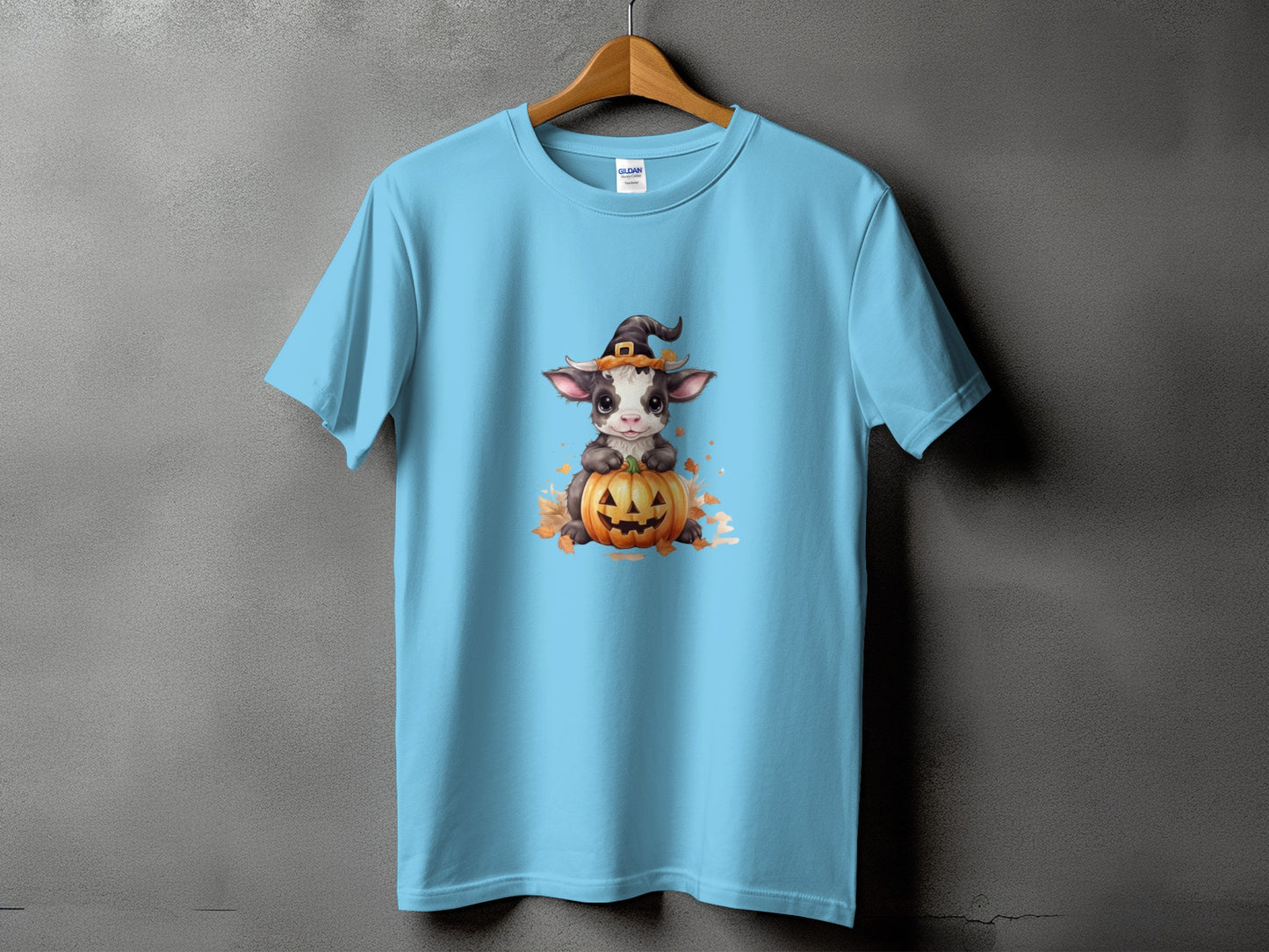 Light blue t-shirt with a cartoon calf wearing a witch hat on a pumpkin.