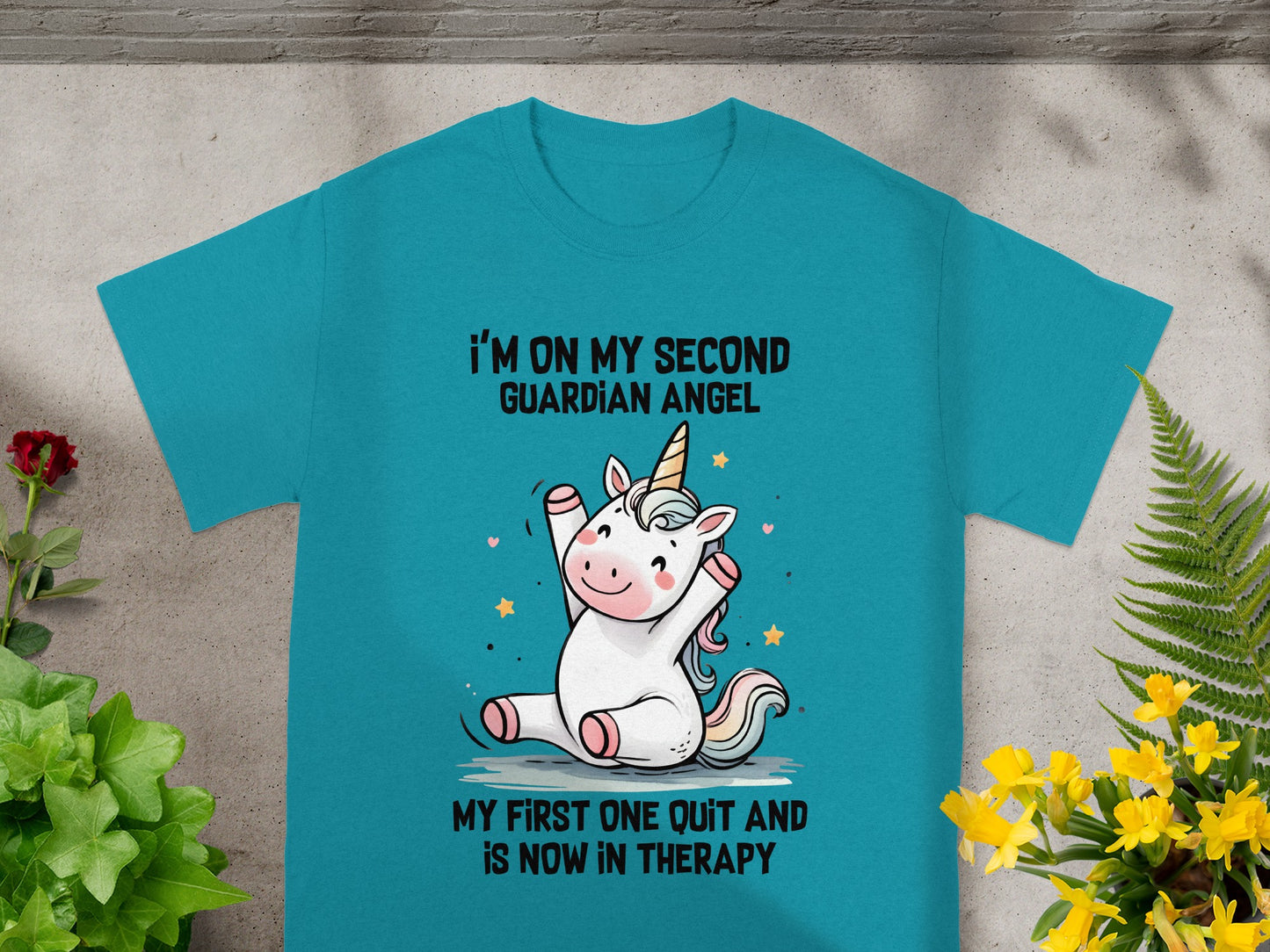 Cyan t-shirt with cartoon unicorn and text: "I'm on my second guardian angel. My first one quit and is now in therapy."