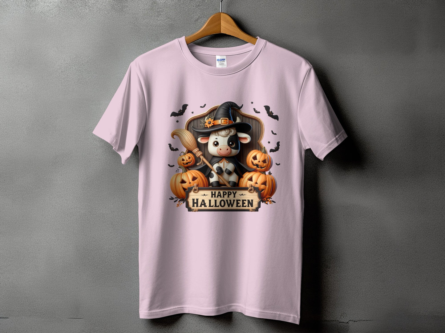 Pink t-shirt with a cow in a witch hat holding a broom and pumpkins, with "Happy Halloween" text.