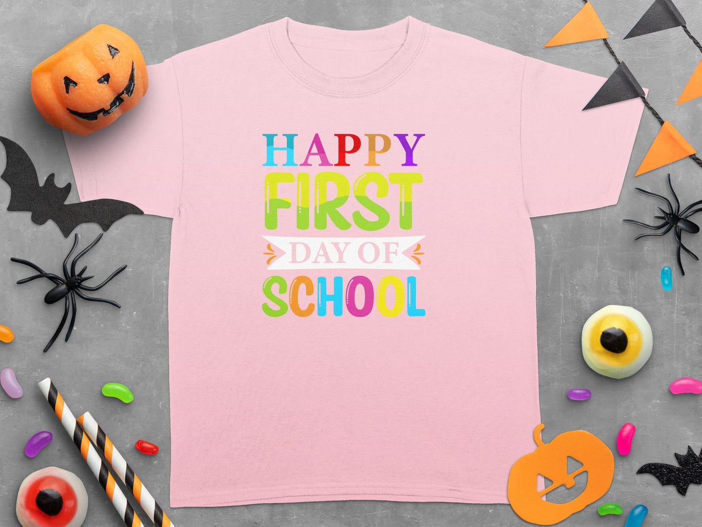 Pink t-shirt reading "Happy First Day of School" with Halloween decorations.