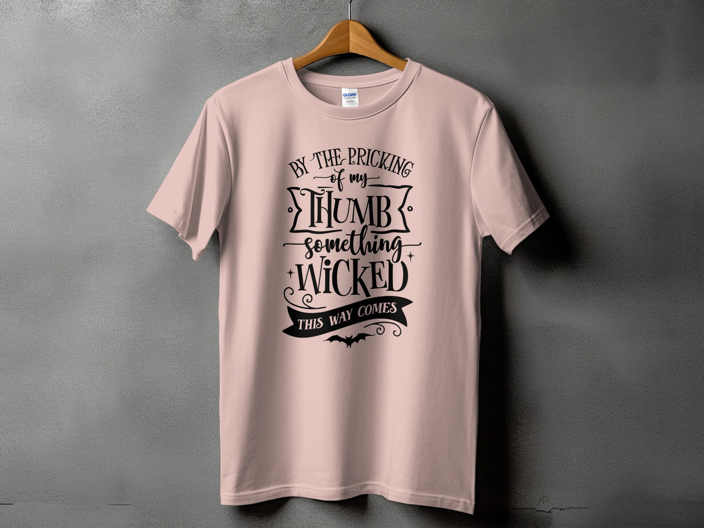 Pink t-shirt with black text "By the pricking of my thumb something wicked this way comes" and a bat graphic.