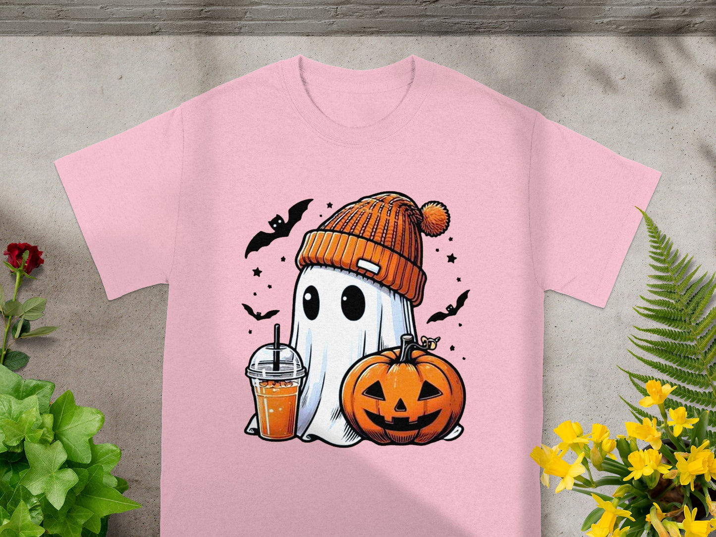 Pink t-shirt with a cartoon ghost wearing a beanie, holding a drink and standing next to a pumpkin.