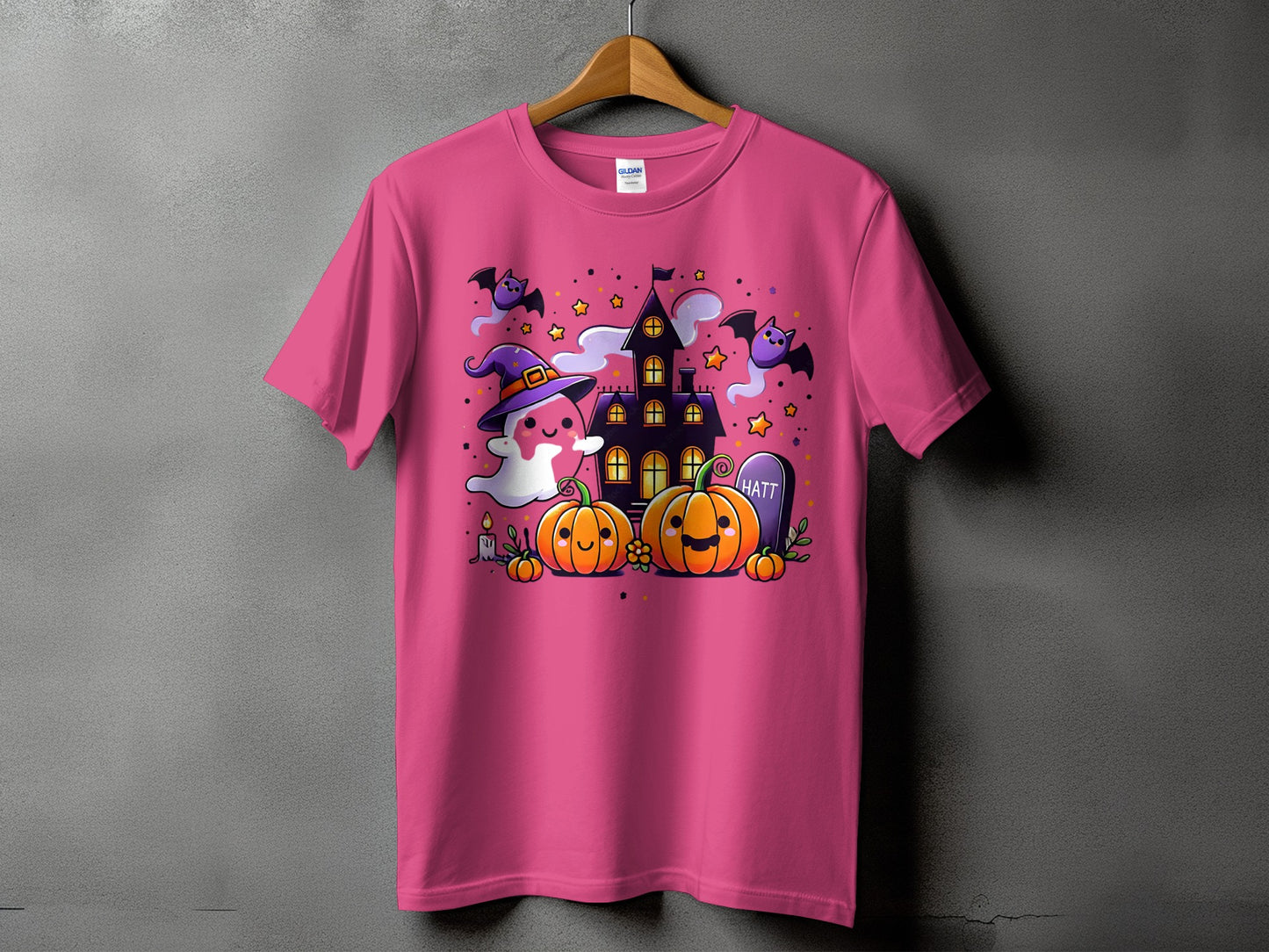 Pink t-shirt with a Halloween graphic featuring pumpkins, a ghost, bats, and a haunted house.
