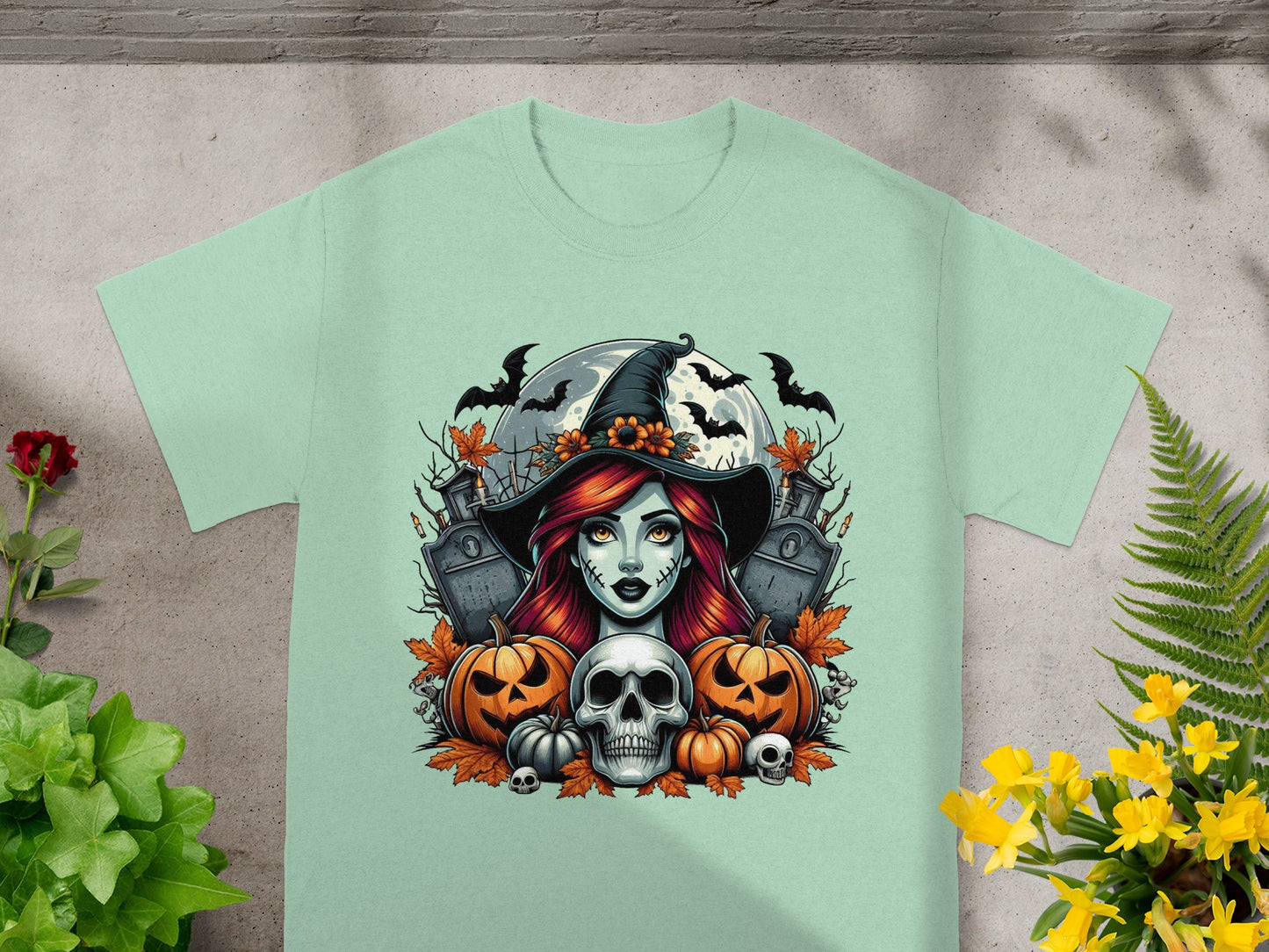 Halloween graphic of witch, skull, pumpkins, bats, and gravestones on a mint t-shirt.