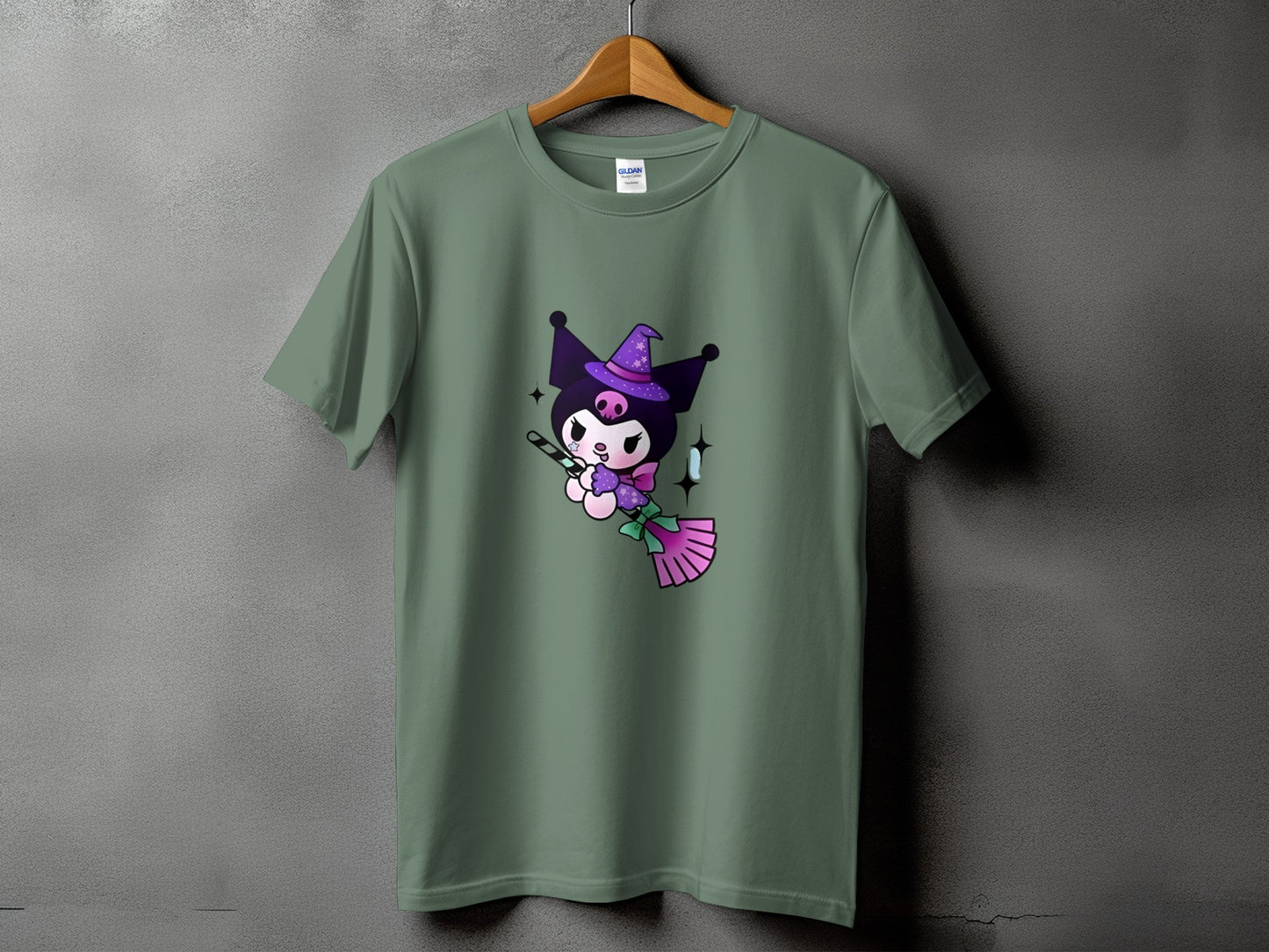 Green t-shirt with a cute cartoon character wearing a witch hat and holding a broom.
