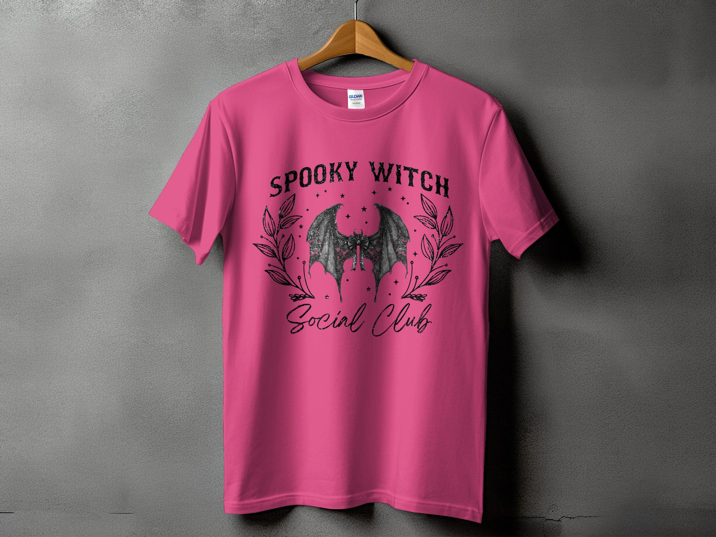 Pink t-shirt with a graphic of bat wings and text "SPOOKY WITCH Social Club".