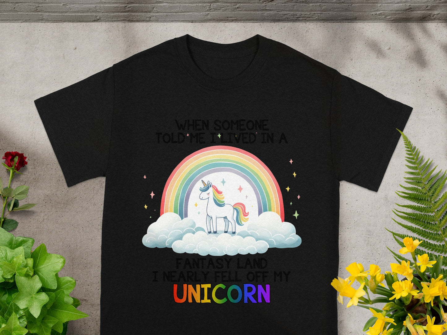 Black t-shirt with unicorn, rainbow, and text "When someone told me I lived in a fantasy land I nearly fell off my unicorn".