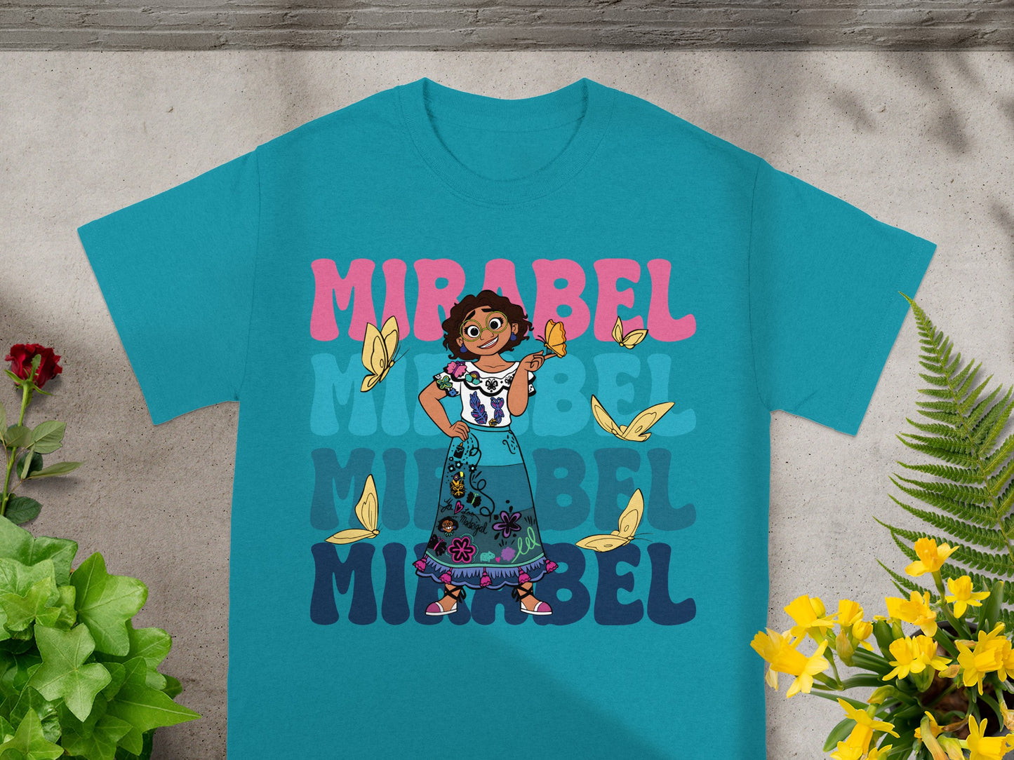 Mirabel from Encanto on a teal t-shirt with colorful butterflies and text.