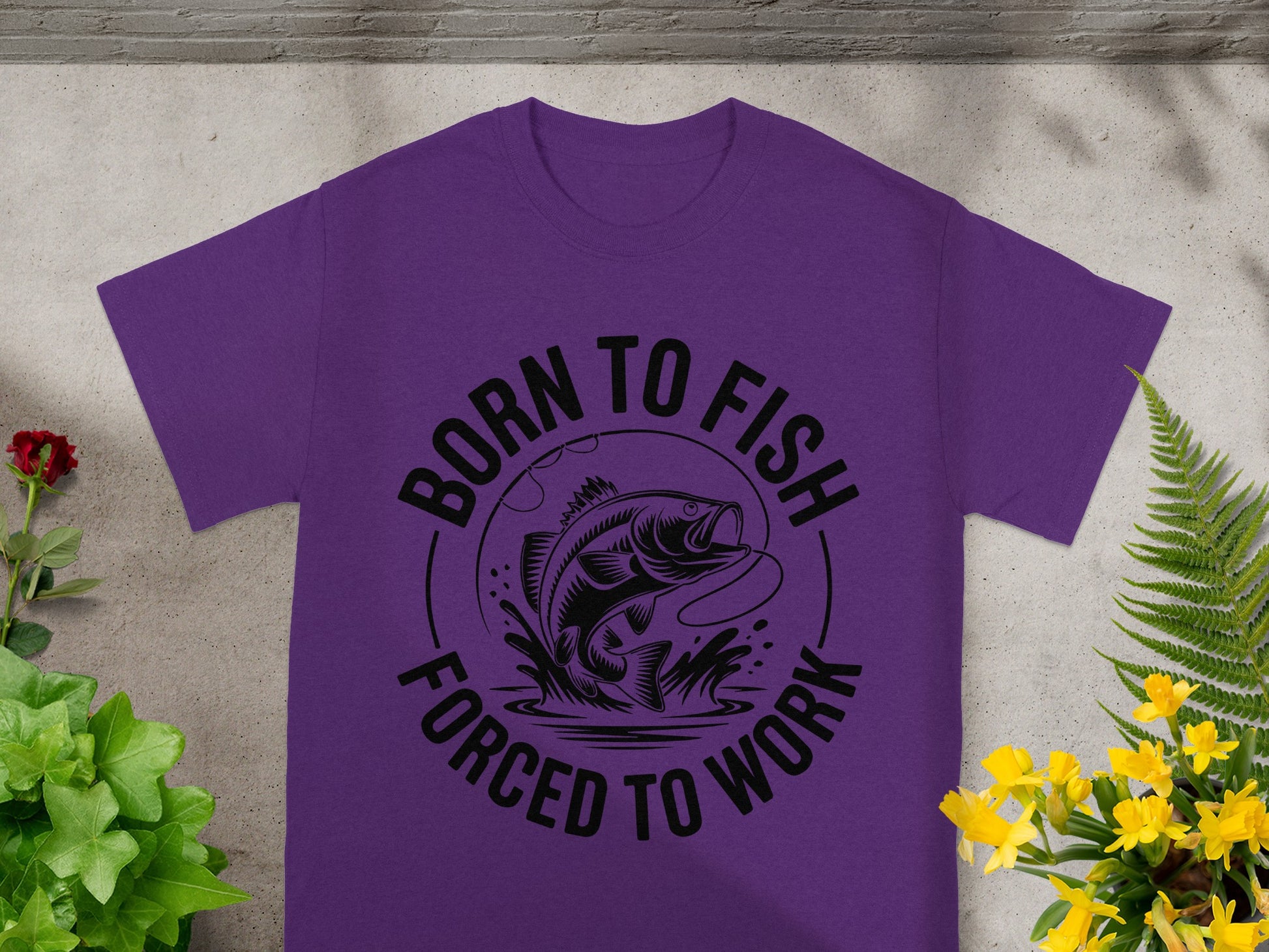 Purple t-shirt with black graphic of a bass fish being reeled in, text reads "Born to Fish, Forced to Work."