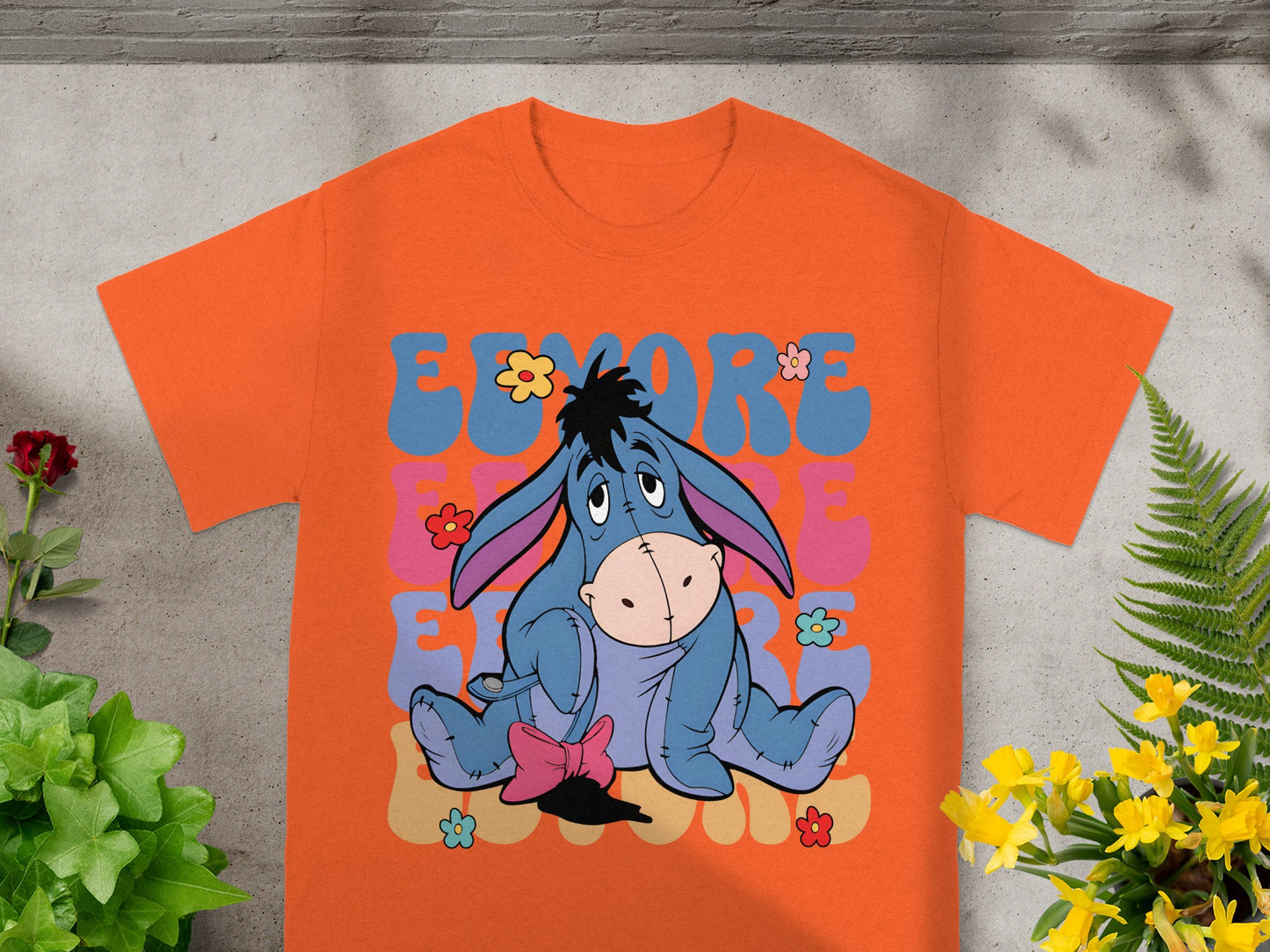 Eeyore character sitting on orange t-shirt with colorful lettering.