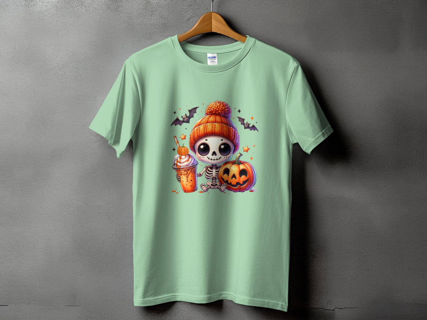 Cute skeleton with pumpkin, drink, bats, and stars on a mint green t-shirt.