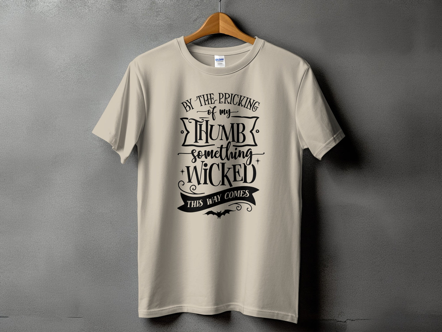 Light tan t-shirt with black text: "By the pricking of my thumb something wicked this way comes."